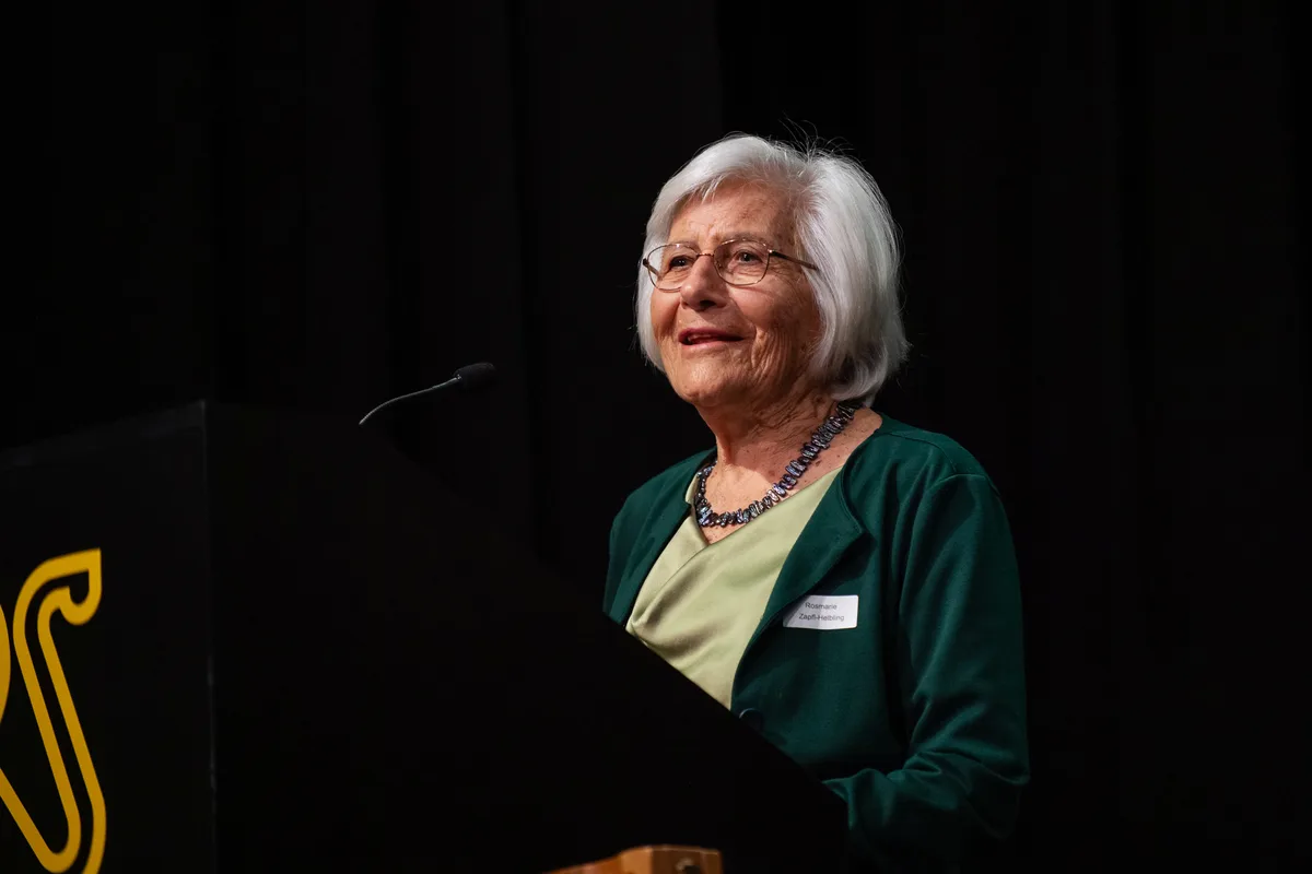 Eine Frau steht an einem Mikrofon und spricht. 